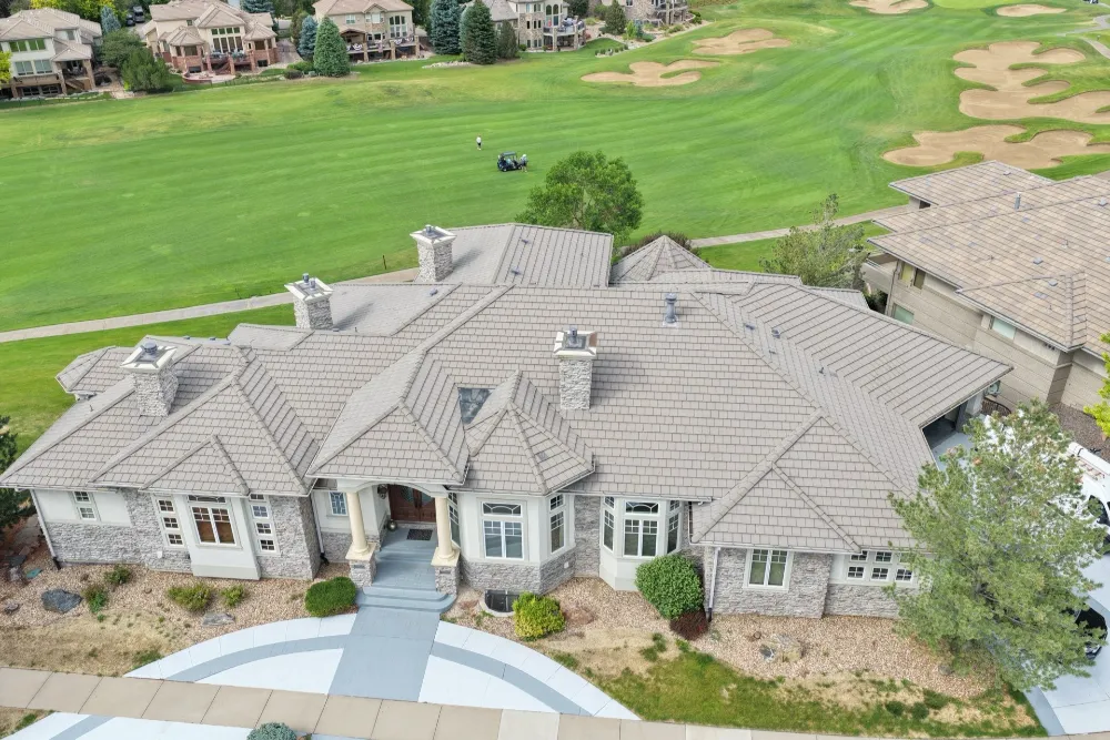 Aerial view of a large home with a multi-gable shingle roof, next to a golf course fairway.