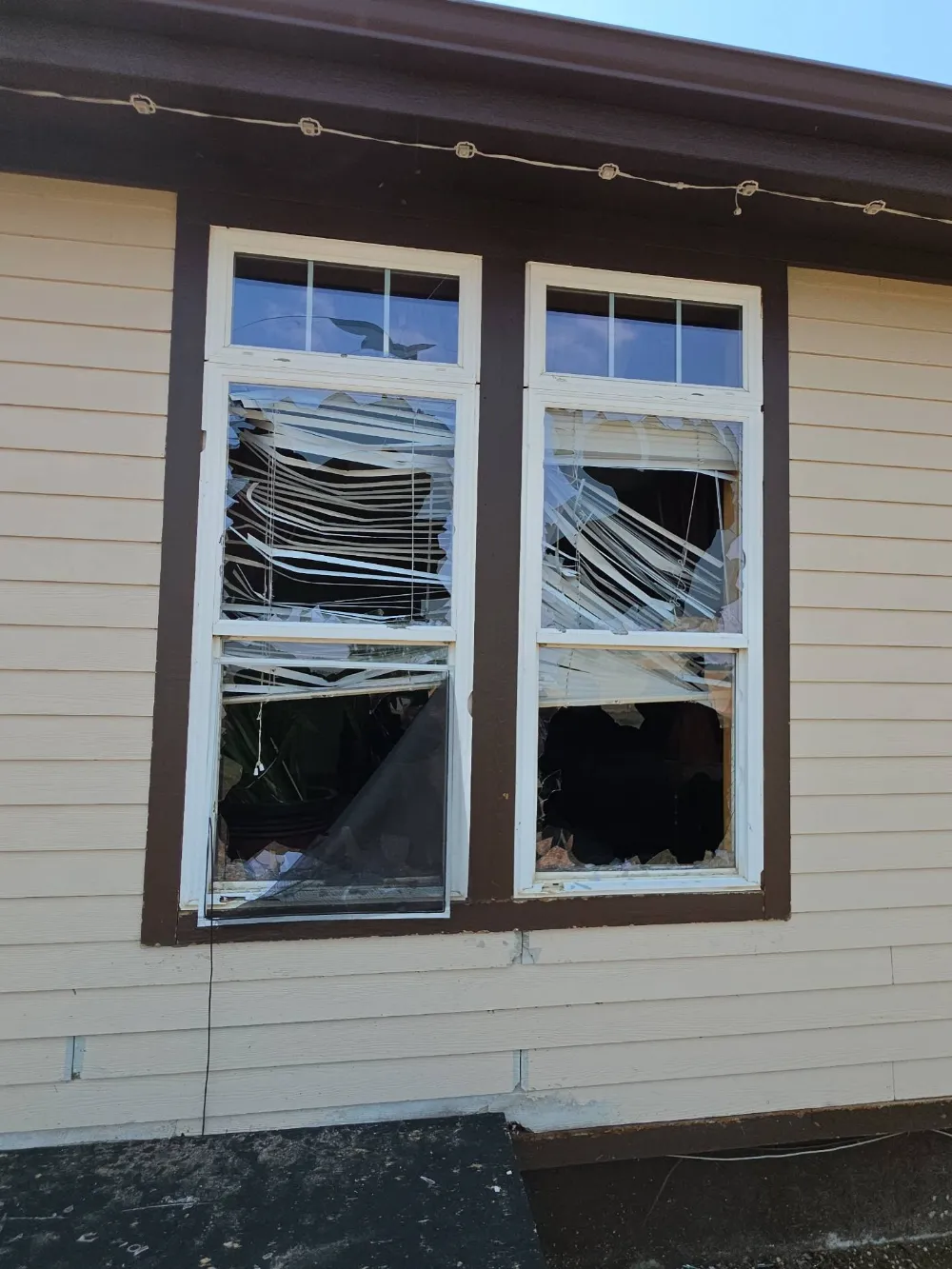 Two broken double-hung windows with shattered glass and damaged blinds