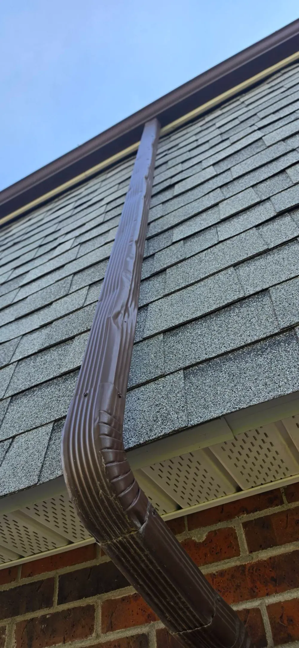 Close-up of a brown metal gutter and downspout along a shingle roofline