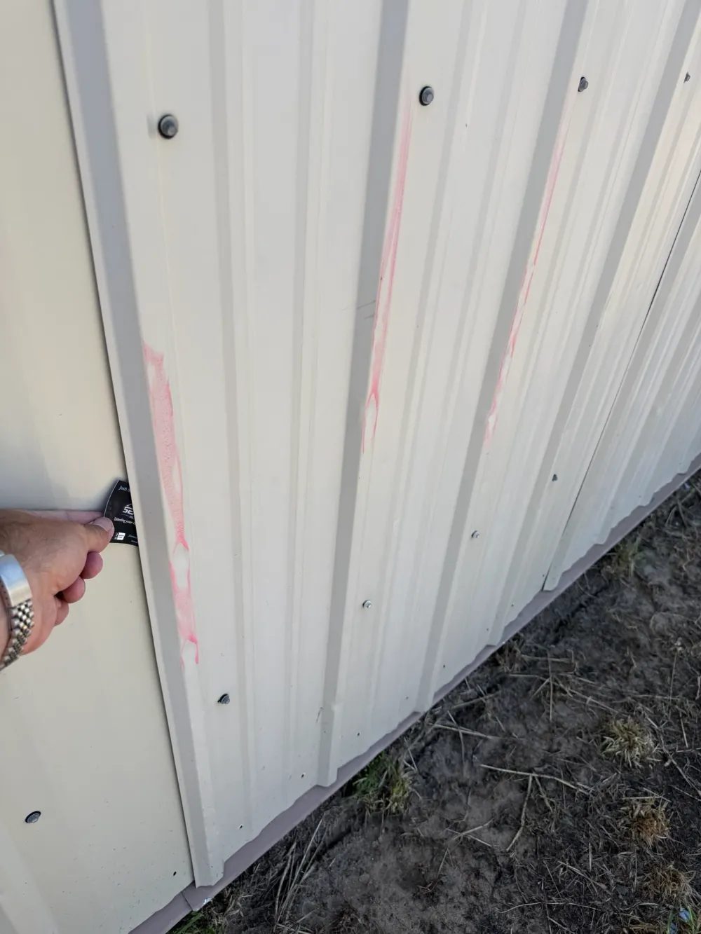 Hand holding a color sample card against a metal panel with chalk markings