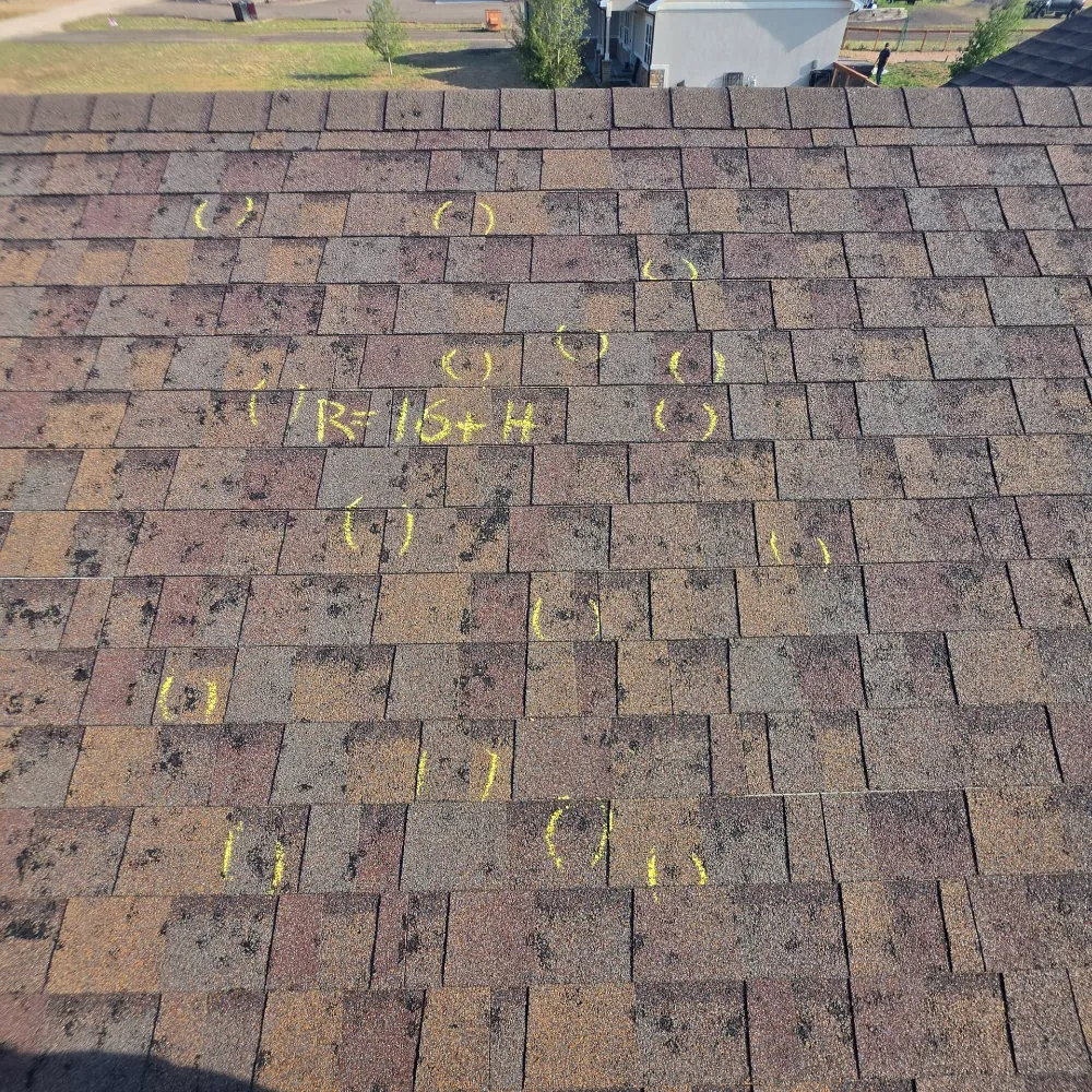 Aerial view of a shingle roof with numerous chalk circles and handwritten notes marked across it.