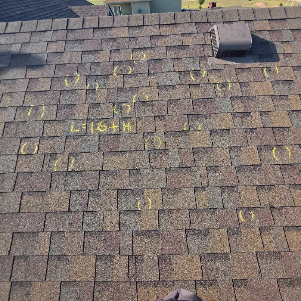 Asphalt shingle roof with chalk circles marking multiple spots and a handwritten measurement note, seen from the rooftop during inspection.